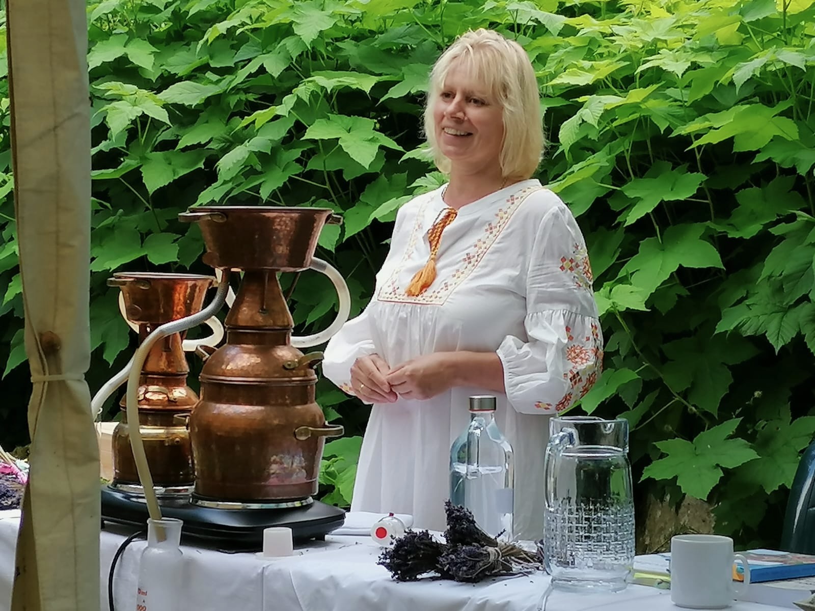Marie in einem weißen Kleid neben einer kupfernen Destillieranlage
